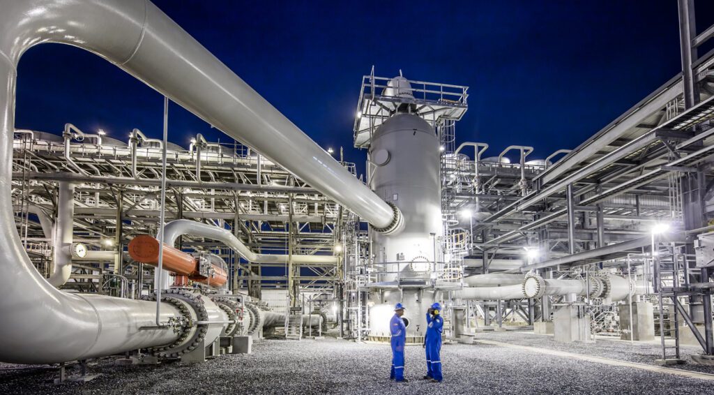 An oil field at night, with two engineers standing in front of it.