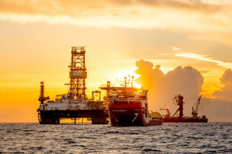 An offshore oil rig and ferry against a sunset backdrop