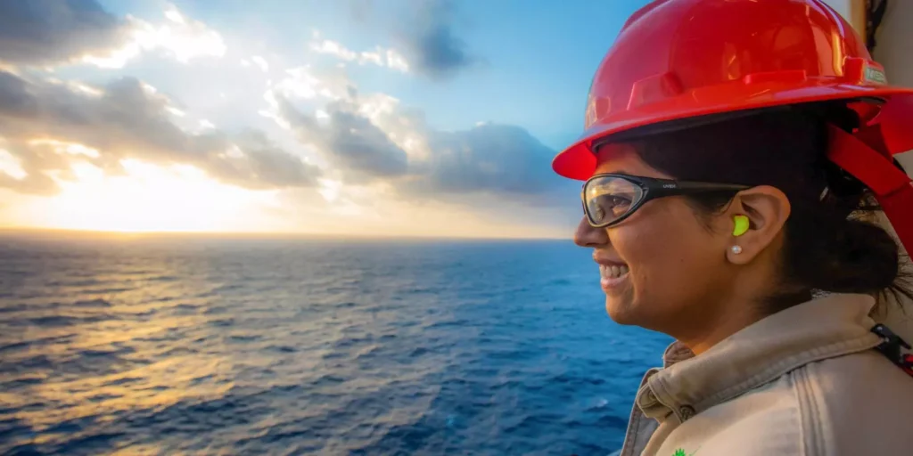 Woman engineer wearing earplugs and red helmet looking out to sea