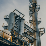 A picture taken from below some chimneys at an oil facility, looking upwards towards the sky.