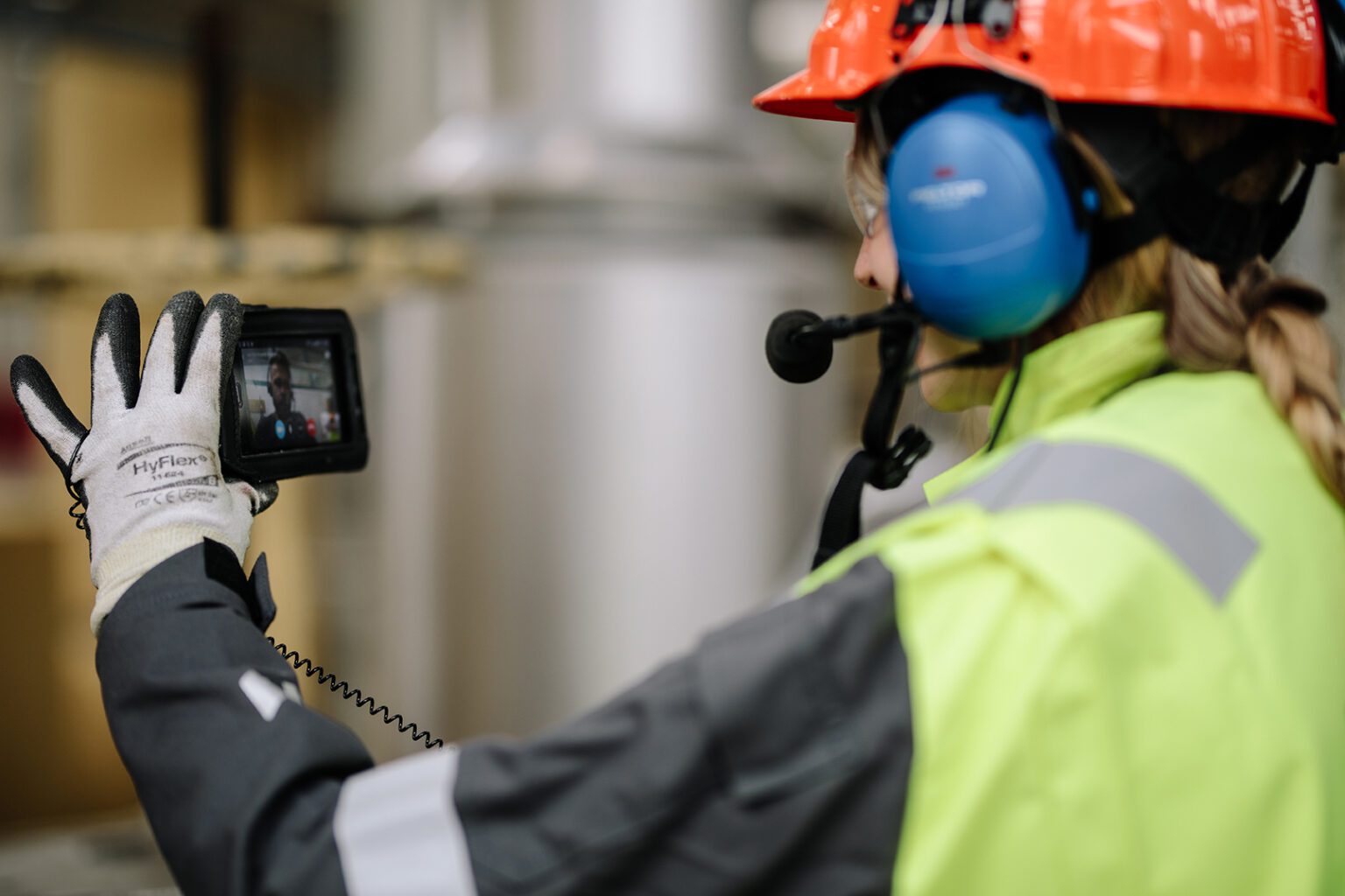 Female digital field worker with hard hat, headphones and hand held device.