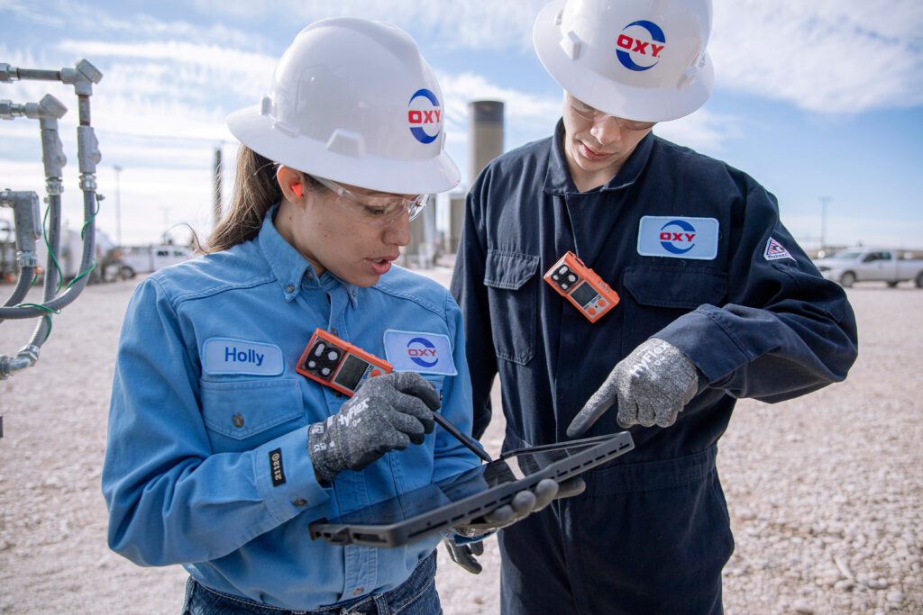 Male and female Oxy engineers working on digital equipment at an oilfield.