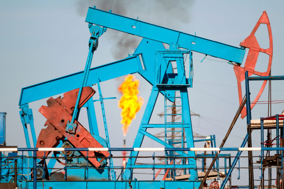 Blue and red equipment at an oil plant with a flare in the background/