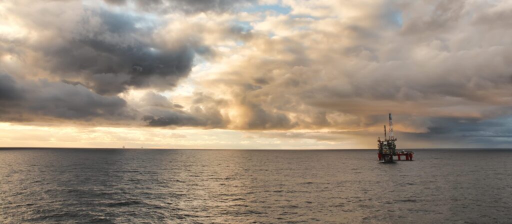 The North Sea with heavy cloud cover and sun breaking through, with a BP oil rig in the distance on the right hand side.