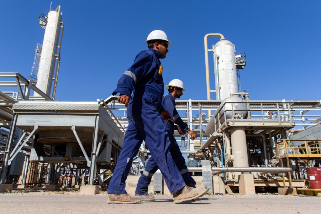 Two engineers in two blue overalls wearing white helmets walking in an oil & gas plant