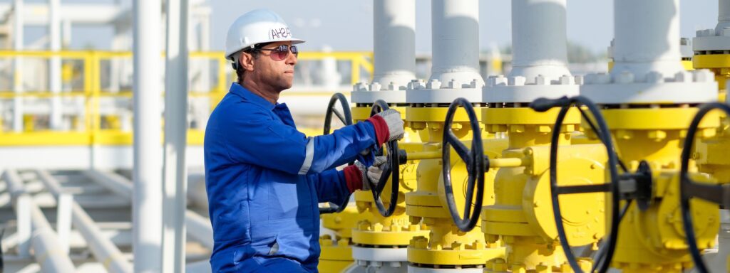 A male engineer working at an oil facility, turning a wheel of a row of bright yellow values.