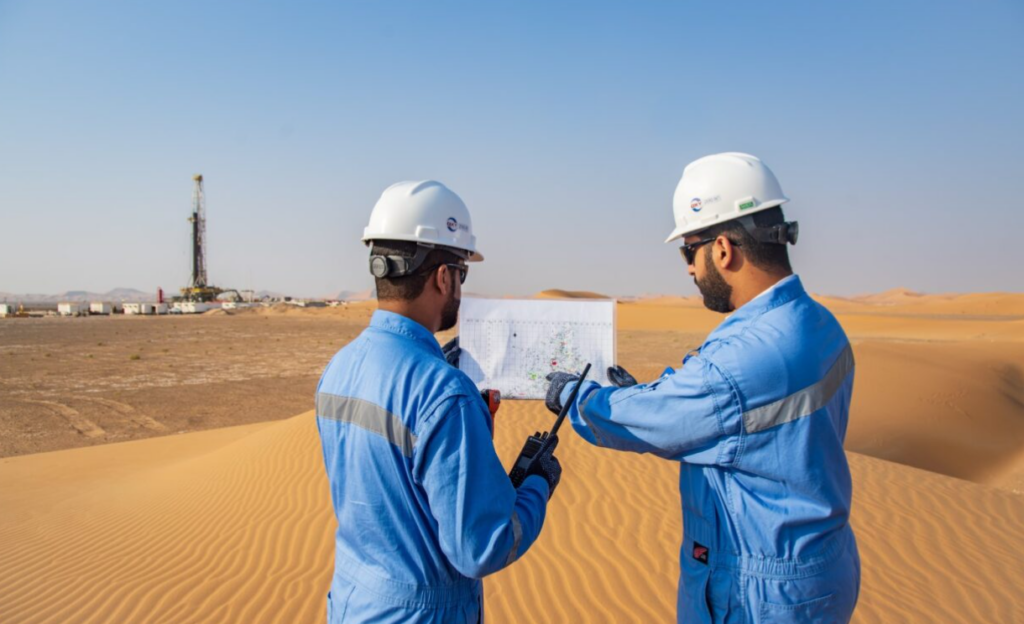 Two engineers working outside of an oil field, looking at some paperwork, in a desert environment.