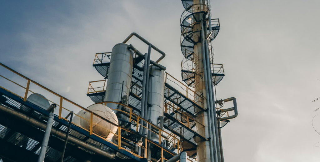 A picture taken from below some chimneys at an oil facility, looking upwards towards the sky.