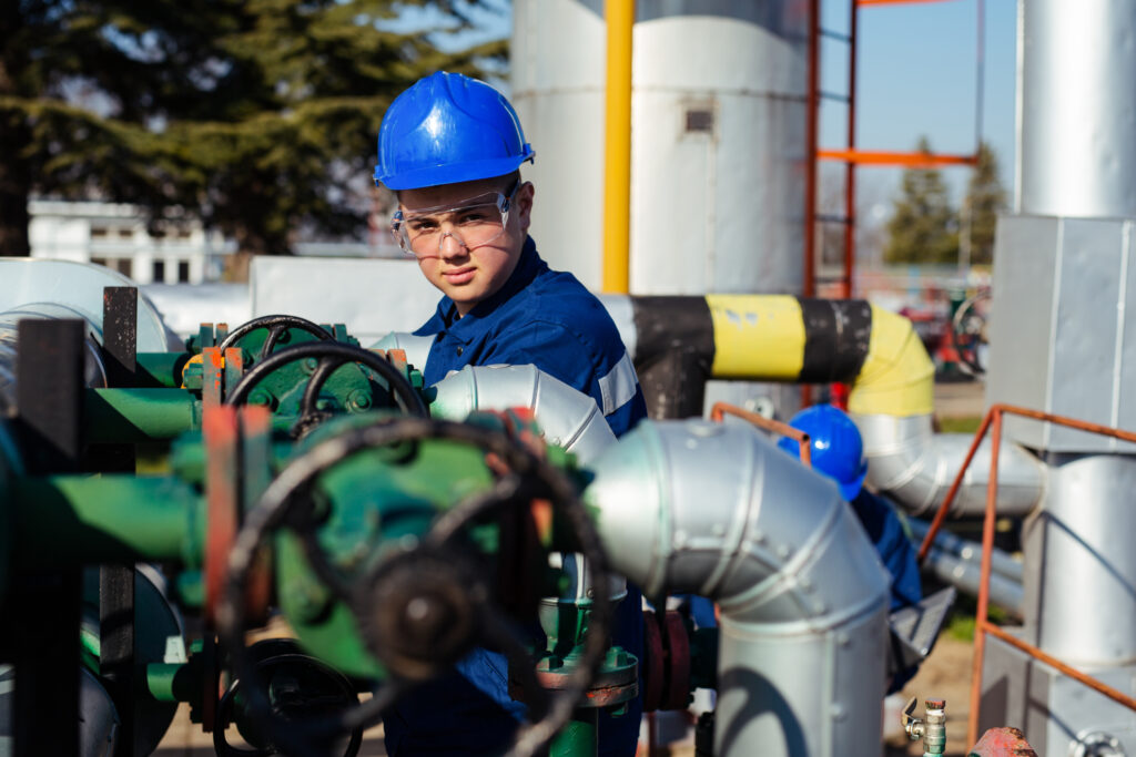 Engineer in a blue hard hat and protective eye wear working on an oil field.